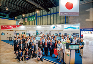 「Singapore Airshow 2024」における高見防衛大臣補佐官(注)と防衛装備庁出展ブース官民関係者の様子(2024年2月)