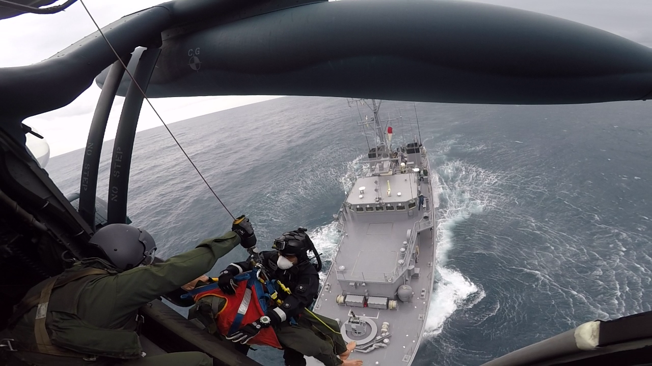 海上自衛隊艦艇からホイスト装置により要救助者を救助する航空自衛隊UH-60Jと救難員