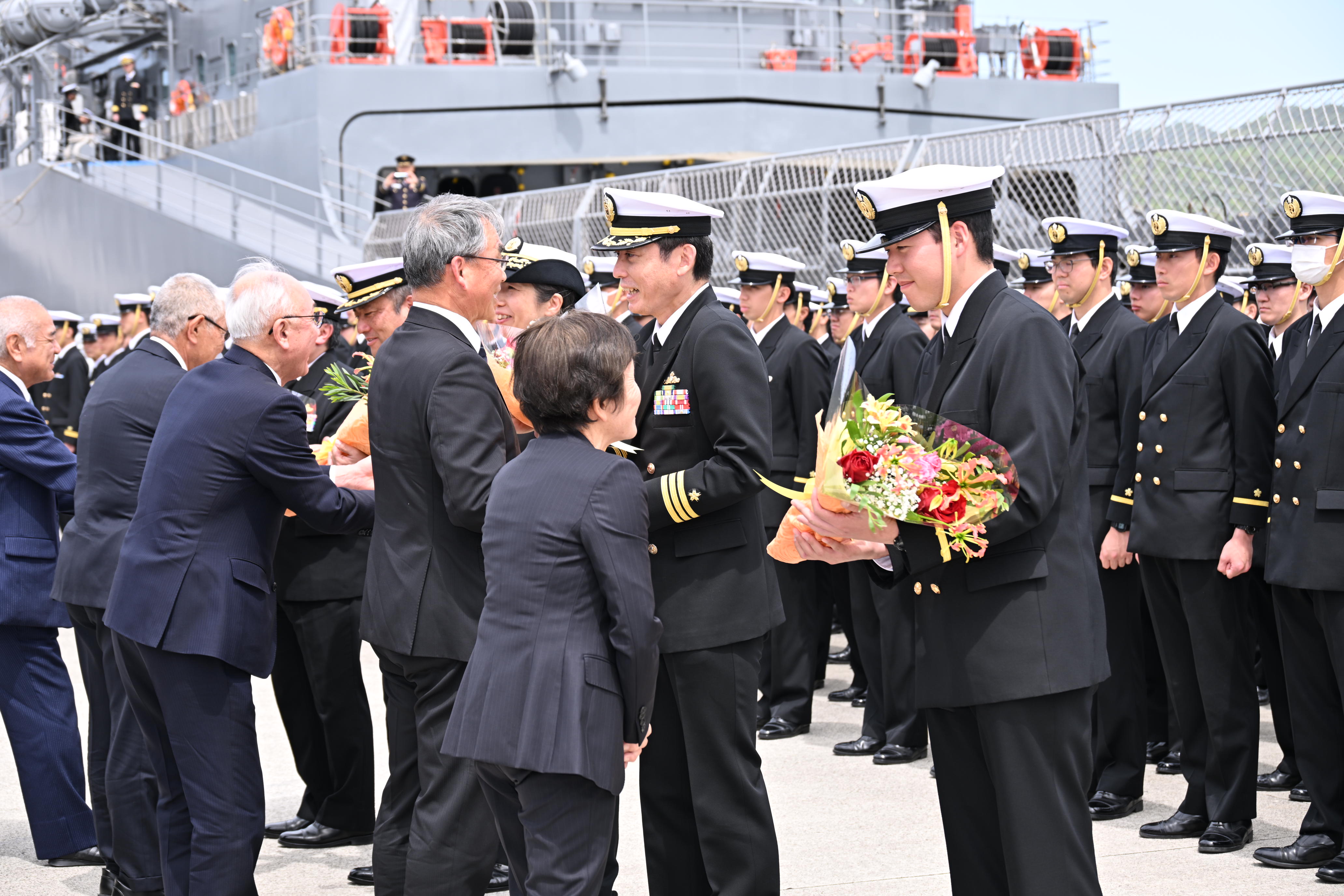 花束贈呈にて笑顔で花束を受け取る練習艦隊司令官、艦長および実習幹部代表